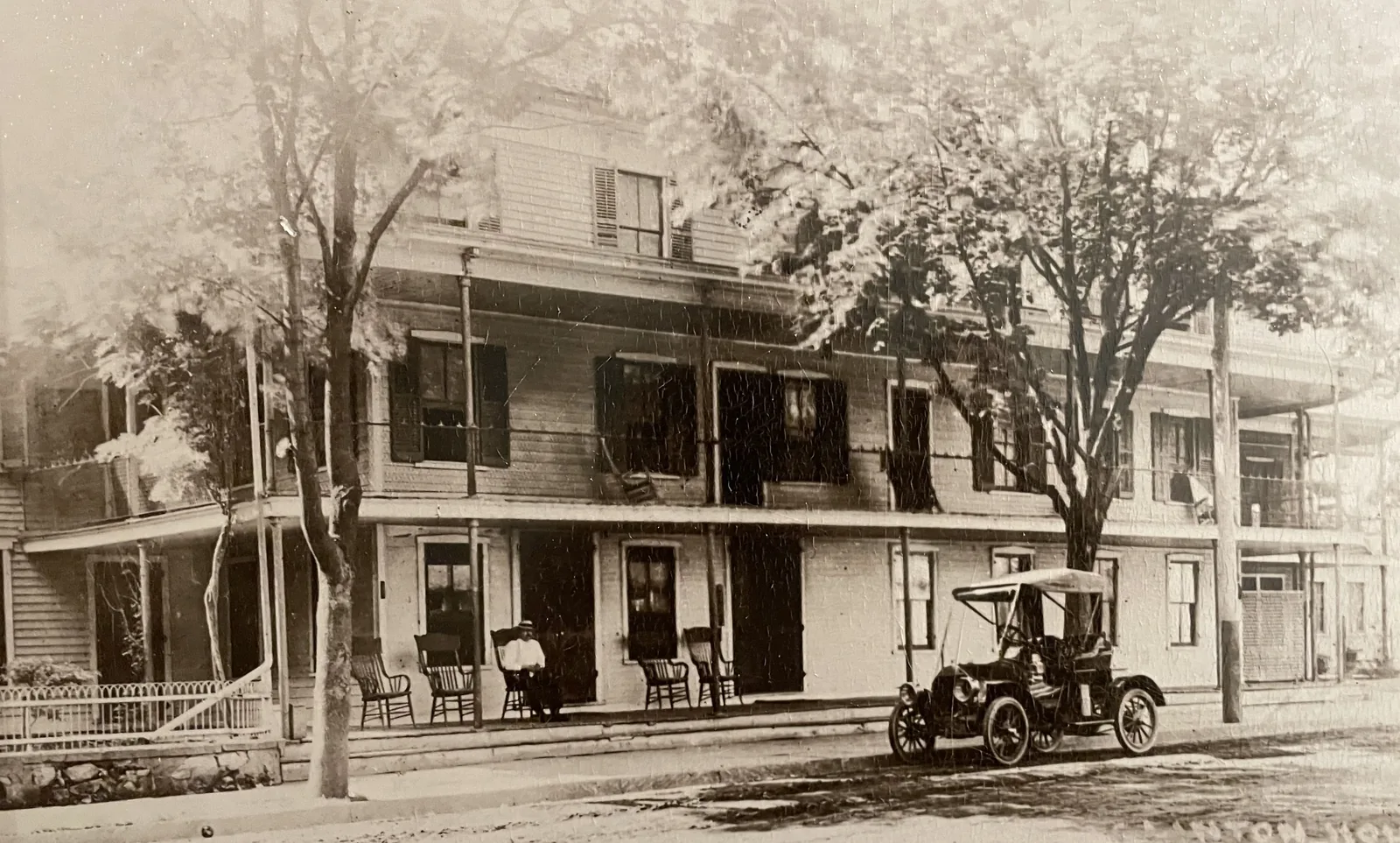 An early motorcar outside the Clinton House, rocking chairs along the porch